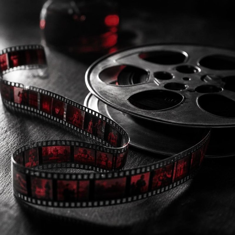 Filmspule mit einem losen Streifen 35-mm-Film auf einem dunklen Tisch (mit AI erstelltes Bild)